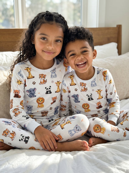 Sister and Brother wearing matching white jungle animal pyjamas with giraffe, lion, Red Panda and Tiger print.