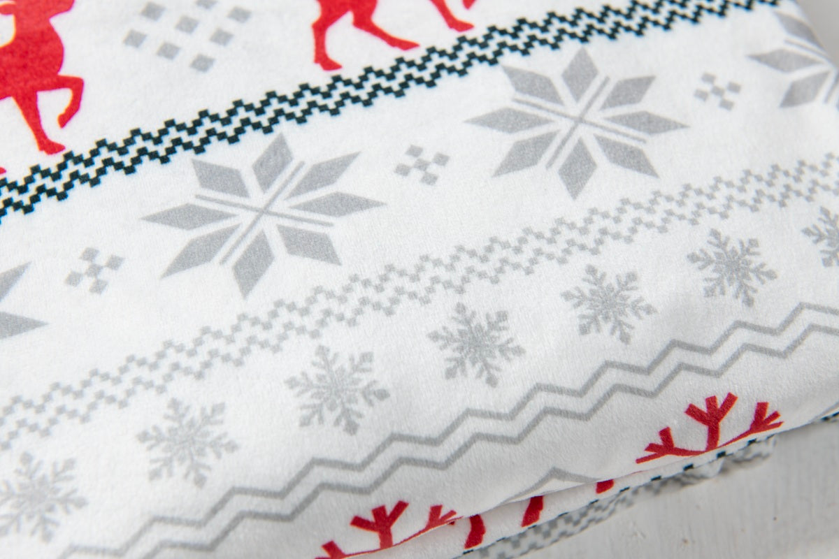 A close-up of a white fabric with a Nordic-style holiday pattern featuring gray snowflakes, red reindeer silhouettes, and geometric borders.