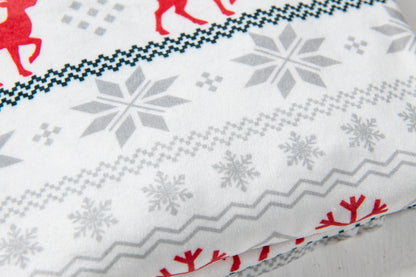 A close-up of a white fabric with a Nordic-style holiday pattern featuring gray snowflakes, red reindeer silhouettes, and geometric borders.