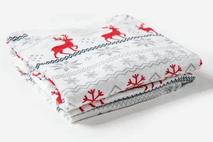 A folded white fabric item, likely a blanket or quilt, featuring a festive Christmas pattern with red reindeer, red snowflakes, and gray snowflake motifs on a white background.