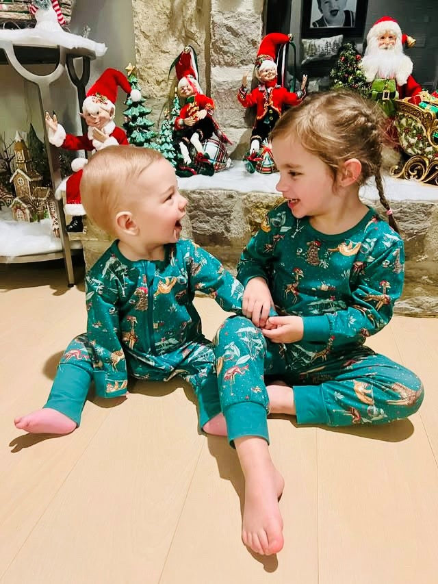 Kids in green jungle print Christmas pyjamas by the fireplace