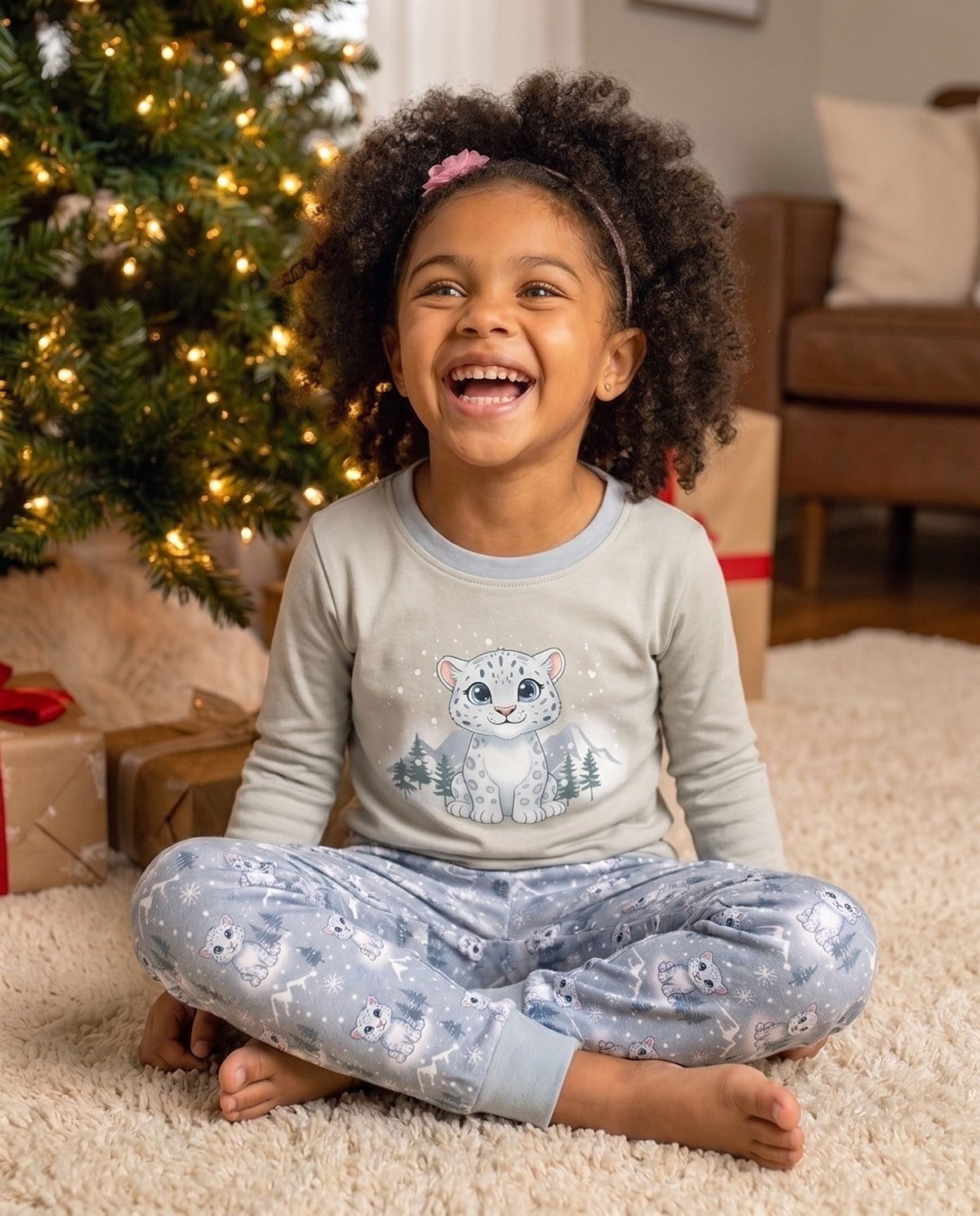 Happy child wearing blue snow leopard Christmas pyjamas with matching trousers in a cosy festive setting.