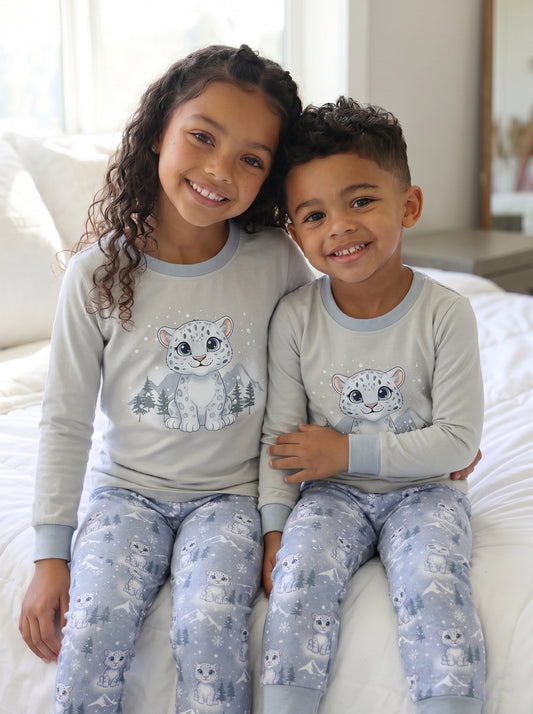 Brother and sister wearing matching blue snow leopard Christmas pyjamas, sitting together indoors in soft cotton festive sleepwear.