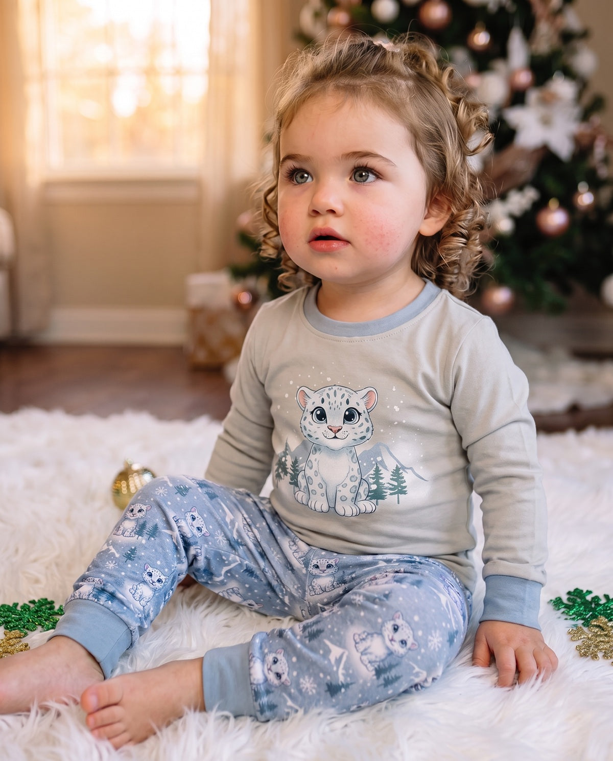 Toddler wearing blue snow leopard Christmas pyjamas sitting indoors in soft cotton festive sleepwear.