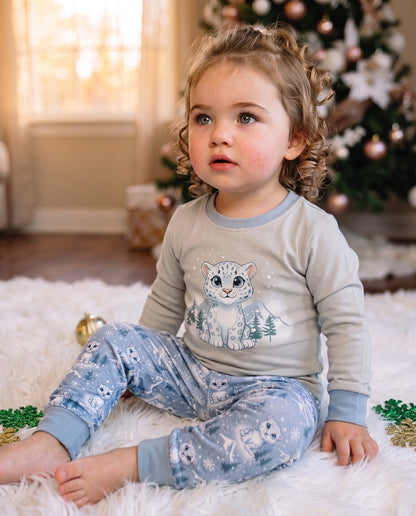 Toddler wearing blue snow leopard Christmas pyjamas sitting indoors in soft cotton festive sleepwear.